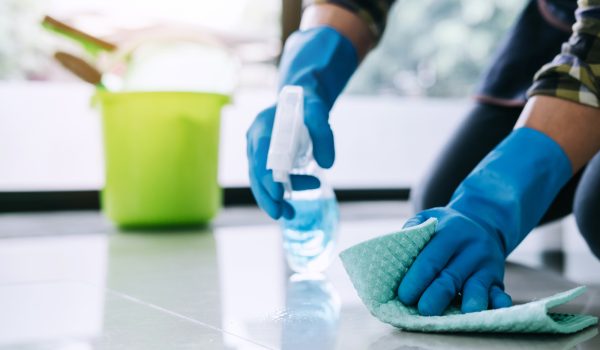 Husband housekeeping and cleaning concept, Happy young man in blue rubber gloves wiping dust using a spray and a duster while cleaning on floor at home.